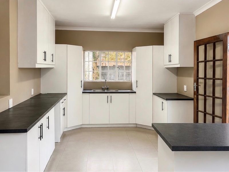 A clean and functional kitchen featuring white cabinetry, dark countertops, tiled flooring, and direct access to the exterior through a timber framed glass door.