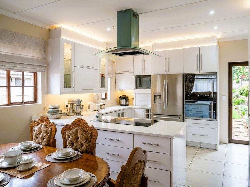 Modern open-plan kitchen featuring white cabinetry, stone countertops, integrated appliances, and a central island with a hob and extractor fan.