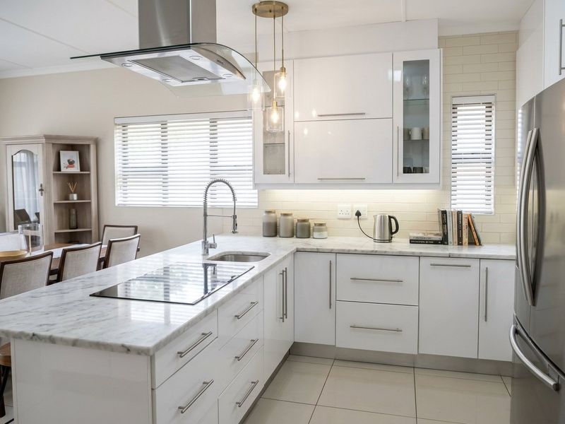Modern kitchen featuring white cabinetry, marble countertops, a central island with an integrated hob, and high-quality stainless steel fixtures.