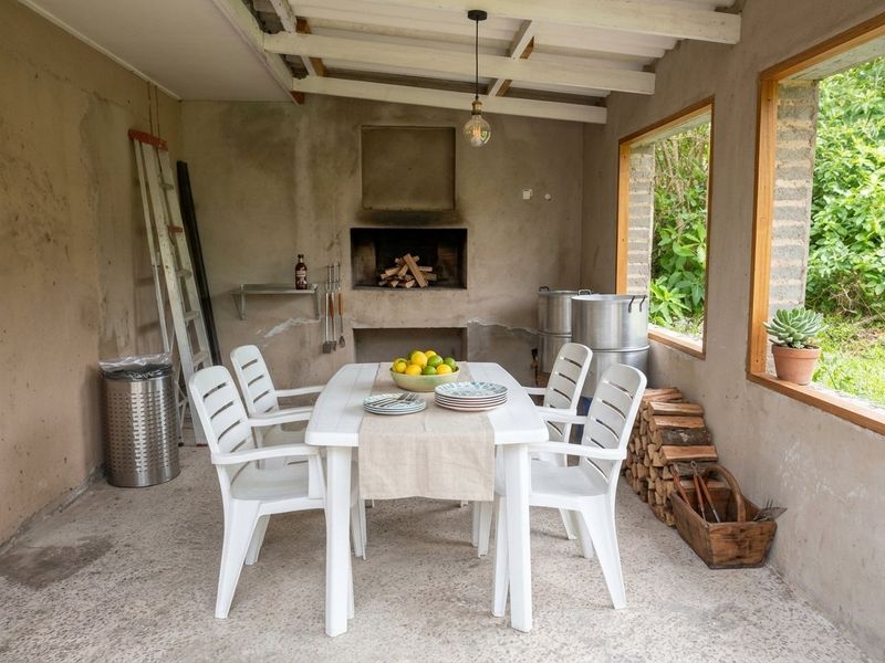 Covered outdoor patio area featuring a built-in braai, exposed beam ceiling, and concrete flooring, offering a rustic space for outdoor dining and entertaining.