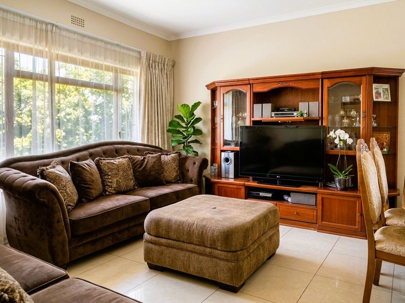 A comfortable living room featuring large windows that provide ample natural light, complemented by neutral tiled flooring and classic cornice detailing.