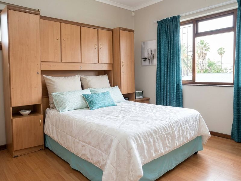 A bedroom featuring built-in wooden cupboards, laminate flooring, and a window with security bars, offering a functional and well-maintained living space.