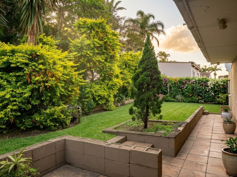 A well-maintained garden featuring a tiled patio area, tiered concrete block retaining walls, and established landscaping with lush greenery.