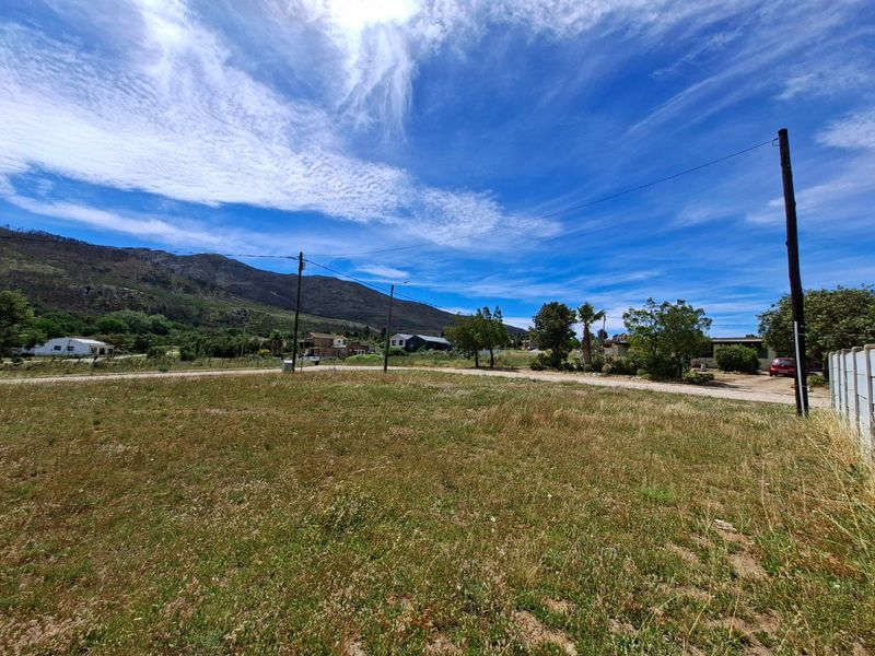 A vacant residential plot featuring open grass, utility poles, and mountain views in a quiet neighborhood setting.