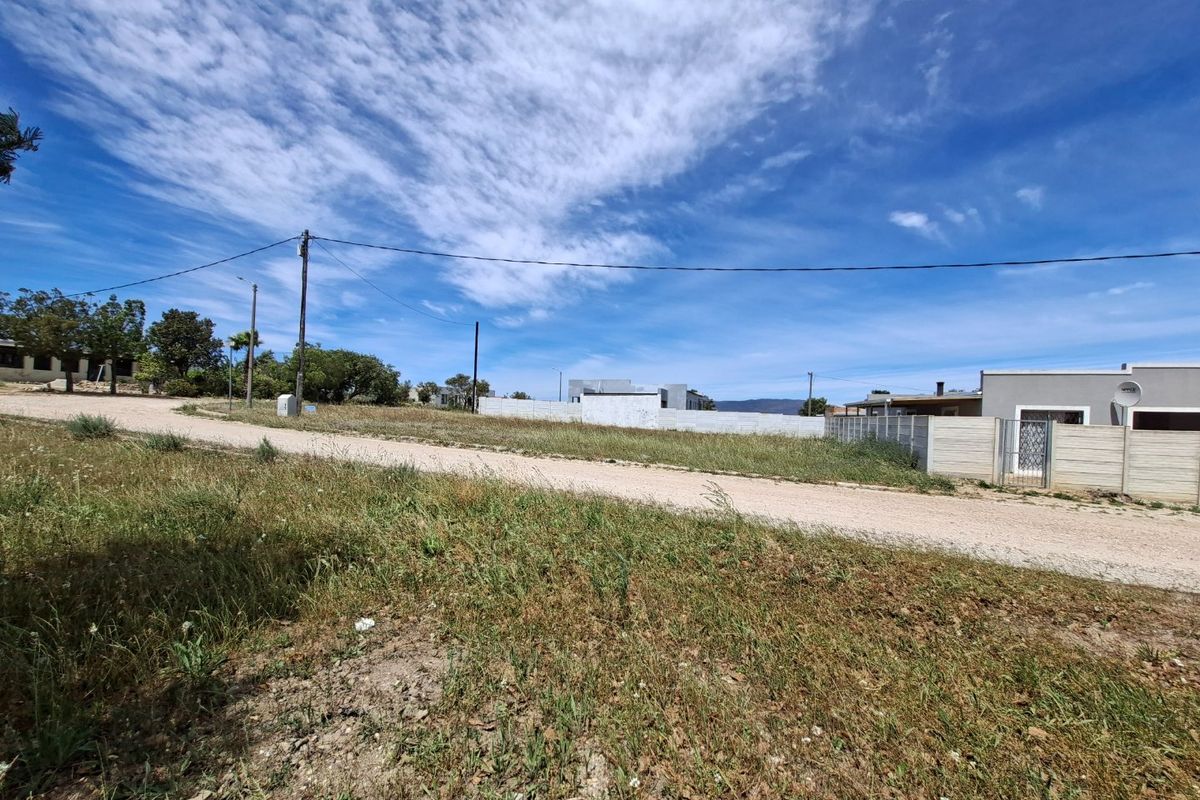 A view of the vacant residential land from the adjacent unpaved street, showing existing boundary walls and utility infrastructure.