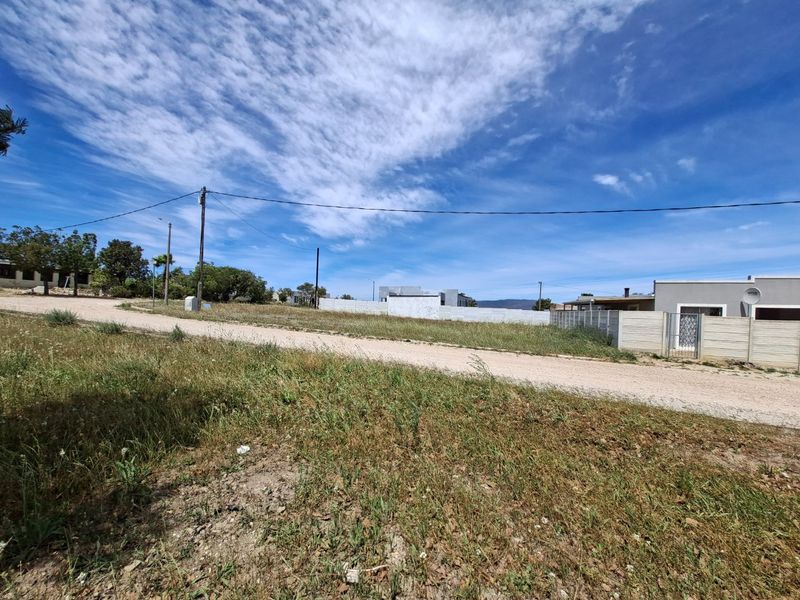 A view of the vacant residential land from the adjacent unpaved street, showing existing boundary walls and utility infrastructure.