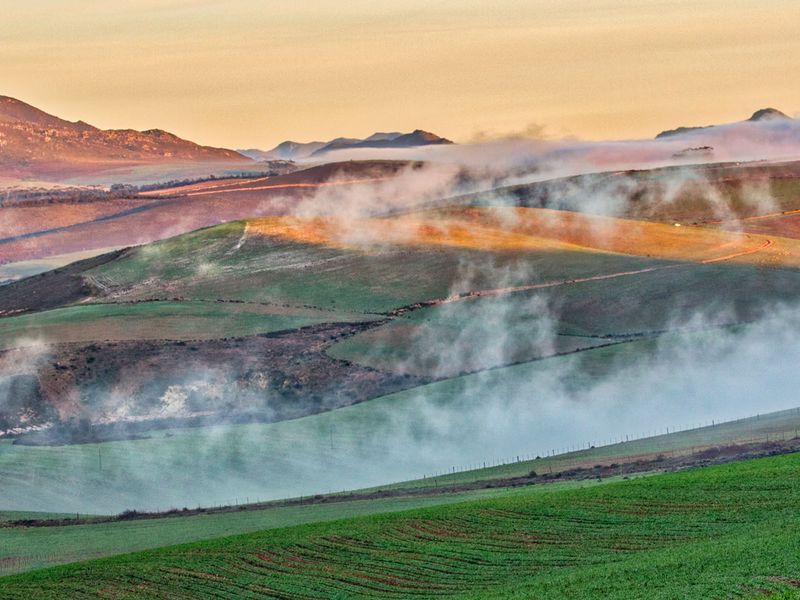 A scenic landscape view of rolling green hills and mountains at sunrise with morning mist.