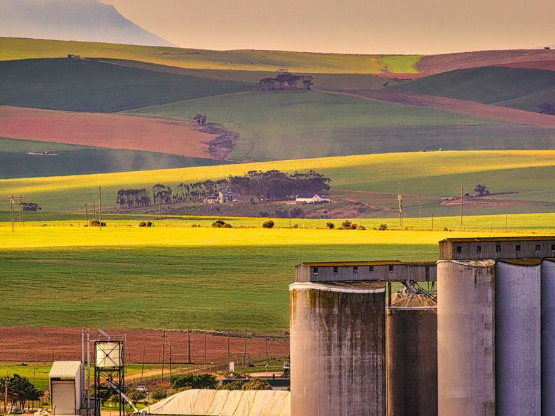 A scenic landscape view featuring agricultural fields, rolling hills, and industrial grain silos in the foreground.