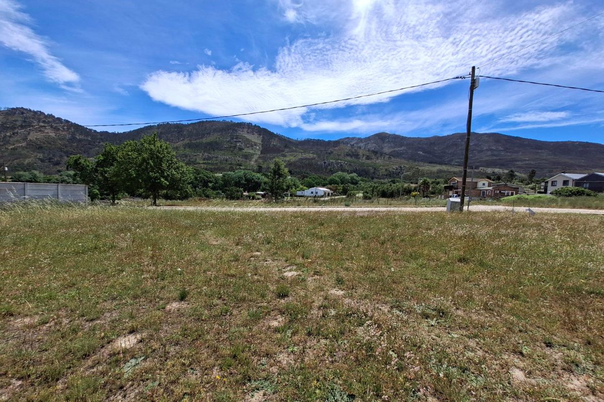 A vacant residential plot featuring natural grass terrain, a boundary wall, and scenic mountain views under a clear blue sky.