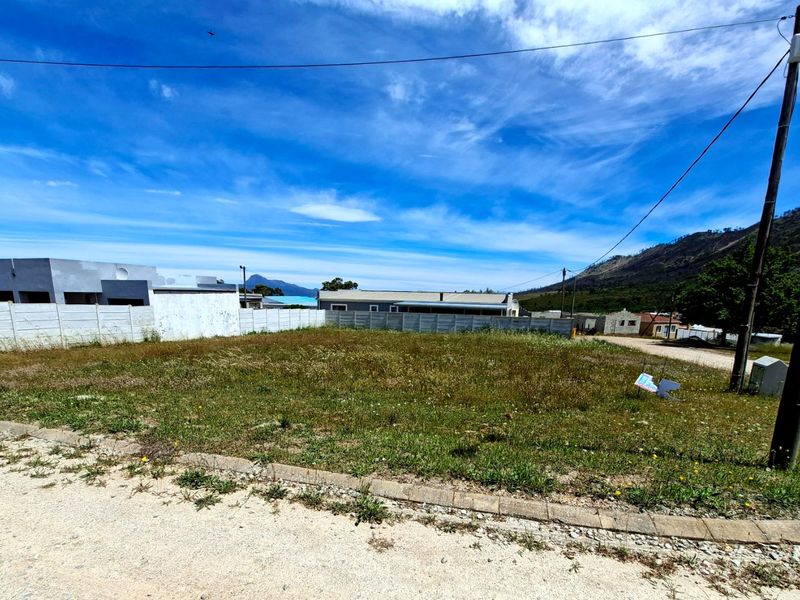 A vacant residential plot featuring a level grassed surface, enclosed by precast concrete boundary walls, with direct access to a gravel road.