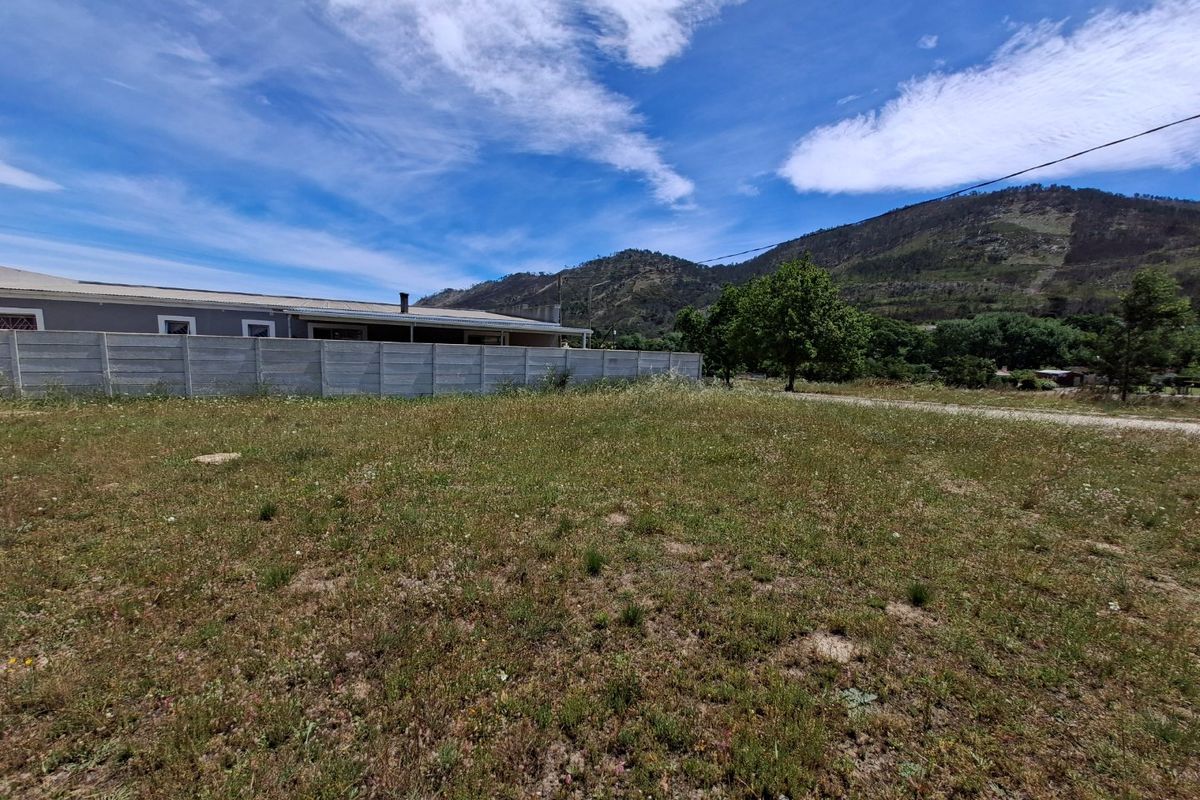 A view of a vacant residential plot featuring a precast concrete boundary wall and scenic mountain backdrop.