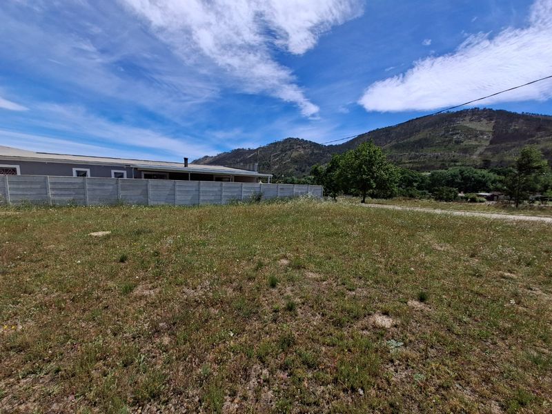 A view of a vacant residential plot featuring a precast concrete boundary wall and scenic mountain backdrop.