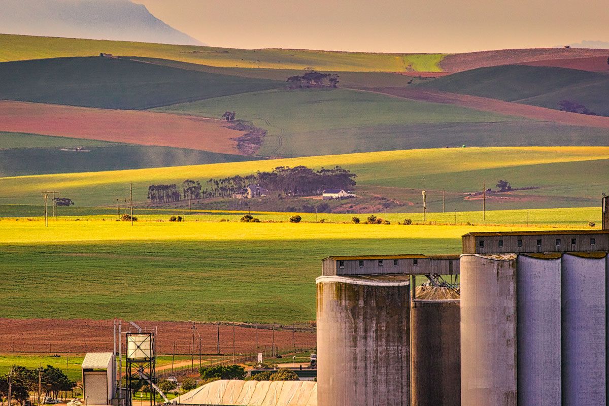 A scenic landscape view featuring agricultural fields, rolling hills, and industrial grain silos in the foreground.