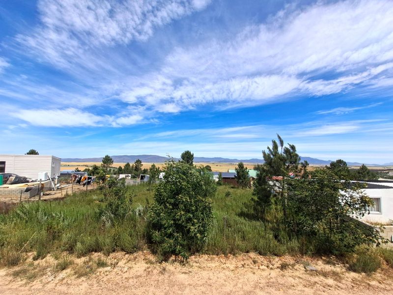 A wide-angle view of a vacant residential plot featuring natural vegetation and distant mountain scenery.