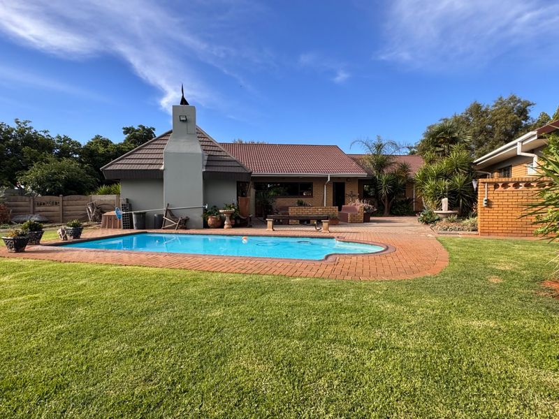 Spacious backyard featuring a swimming pool with brick paving, an outdoor fireplace, and a well-maintained lawn area.