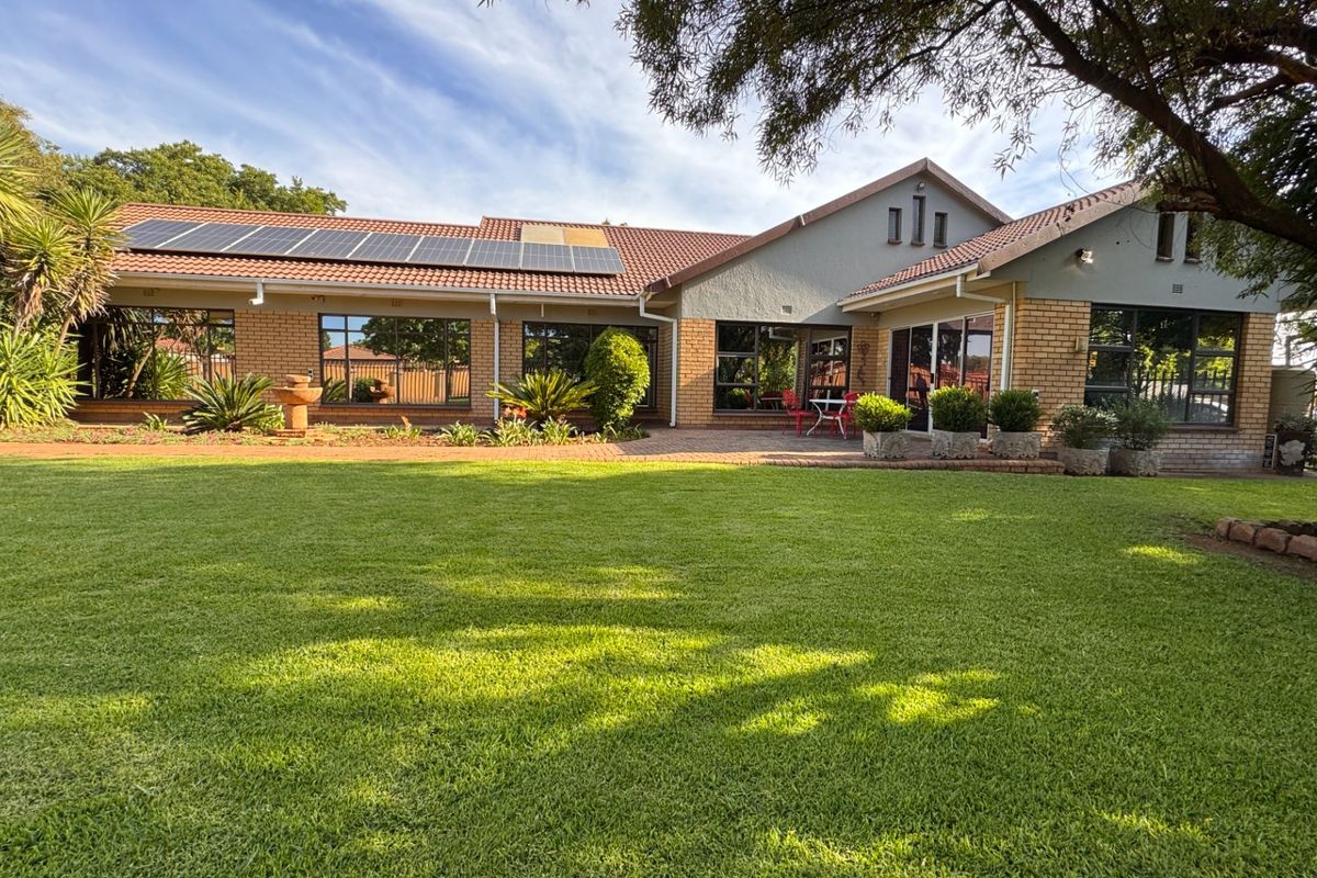 A well-maintained rear exterior view featuring a spacious lawn, paved patio area, brick facade, and roof-mounted solar panels.