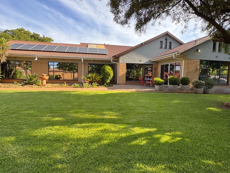 A well-maintained rear exterior view featuring a spacious lawn, paved patio area, brick facade, and roof-mounted solar panels.