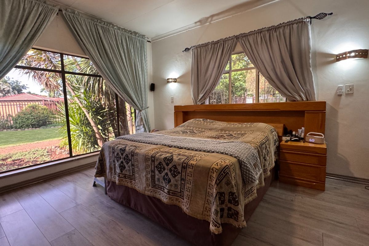 Spacious bedroom featuring laminate flooring, built-in headboard, and large windows providing natural light and garden views.