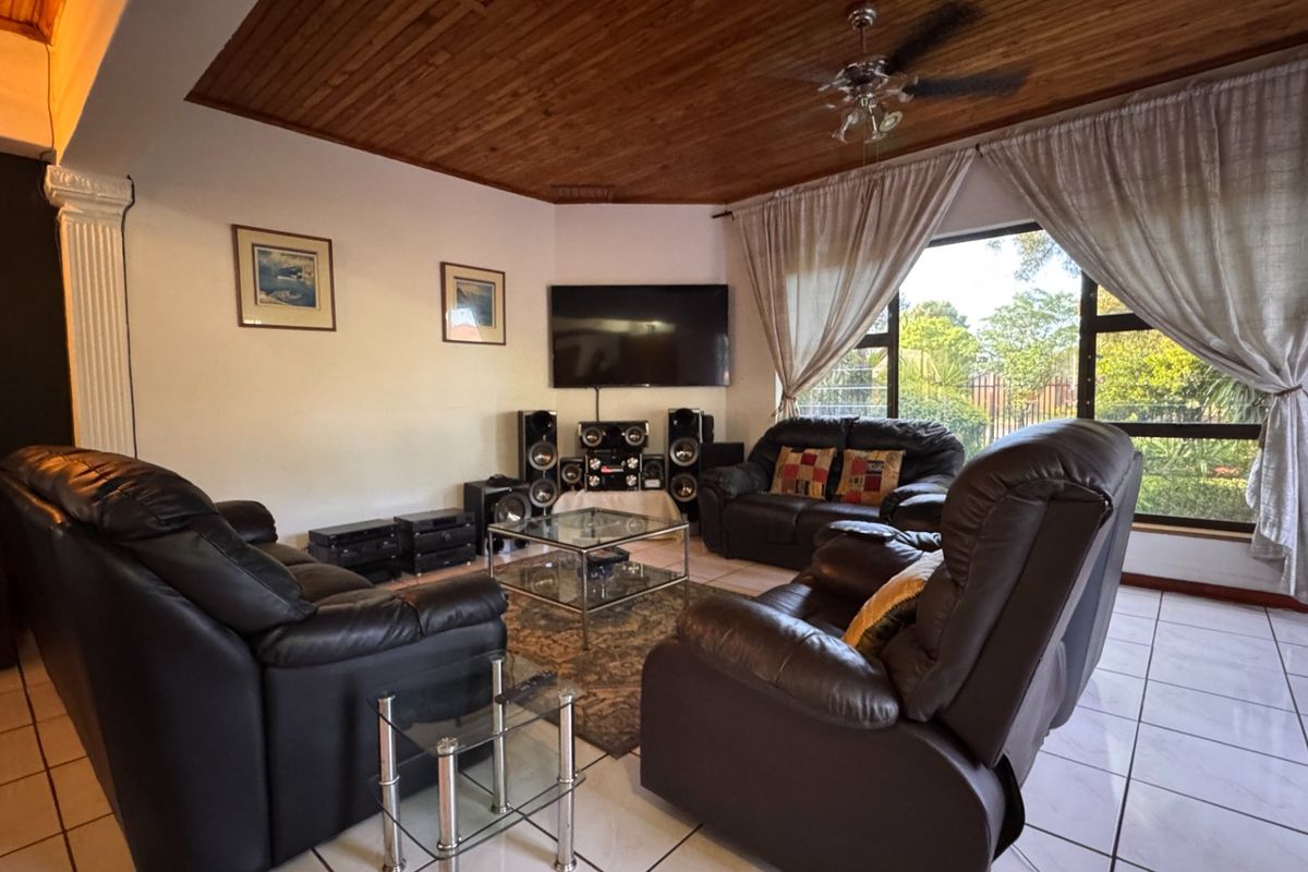 Spacious living room featuring a warm timber tongue and groove ceiling, ceiling fan, and large windows that provide ample natural light.