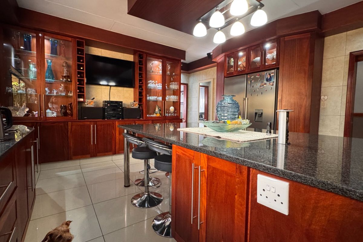 Spacious kitchen featuring dark wood cabinetry, granite countertops, a central island, and integrated display shelving, offering a warm and functional culinary space.