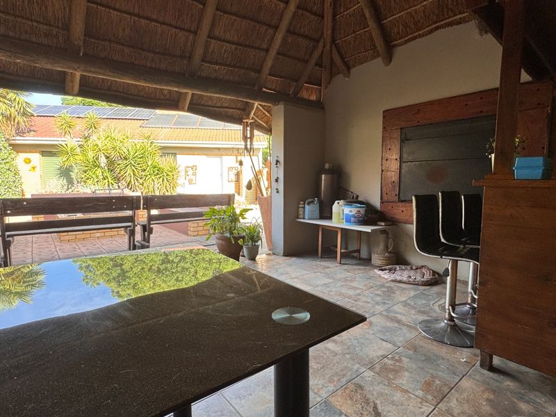 Covered outdoor patio area featuring a traditional thatched roof, tiled flooring, and a built-in braai, perfect for relaxed outdoor entertaining.