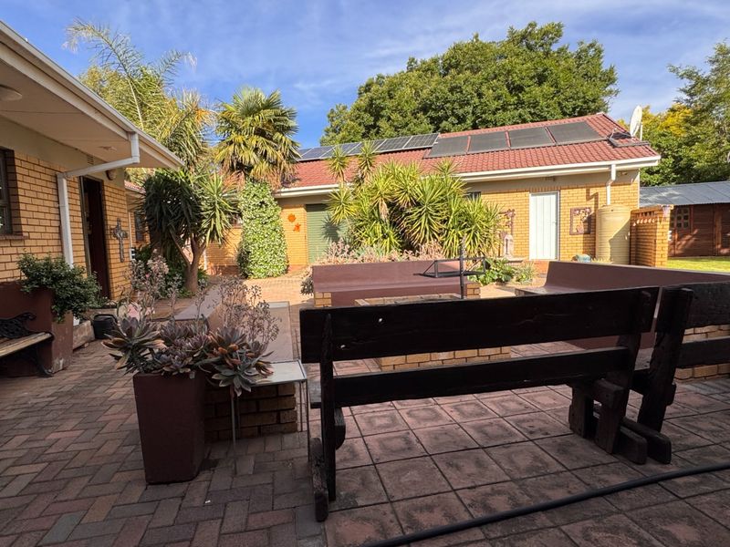 Rear courtyard area featuring brick paving, built-in seating, and a brick-built structure with solar panels installed on the roof.