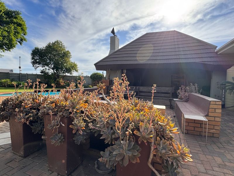 Outdoor patio area featuring brick paving, a built-in brick bench, and a covered section with a chimney, overlooking the swimming pool and garden.