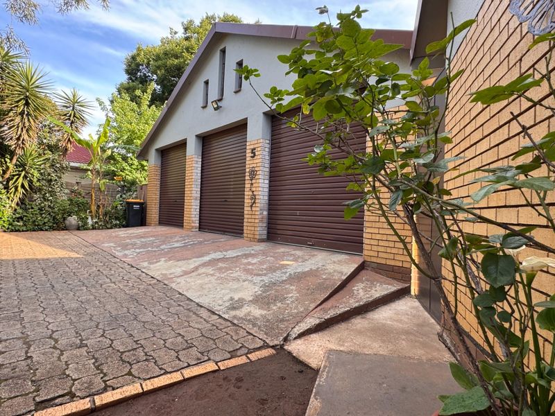 A triple garage with roller doors and a paved driveway, featuring a brick and rendered facade.