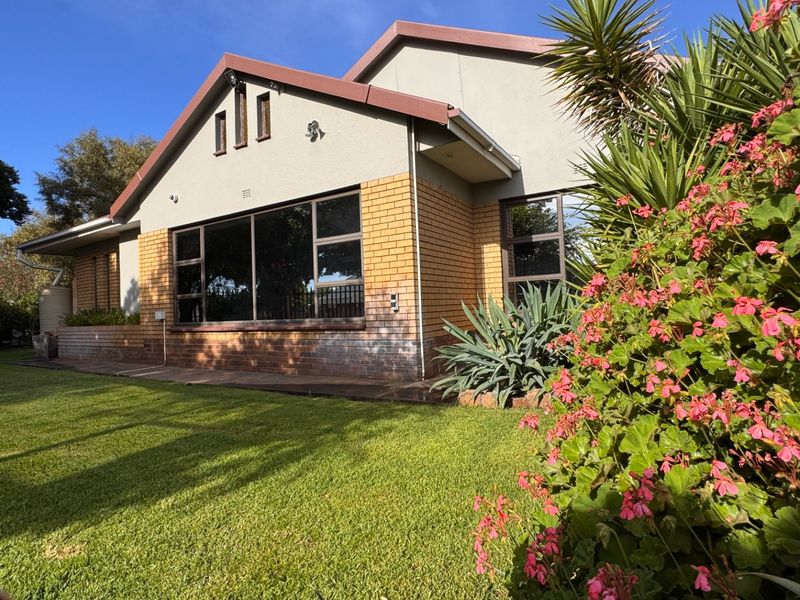 Rear view of the house featuring a well-maintained garden, brick and plaster facade, and large windows providing natural light.