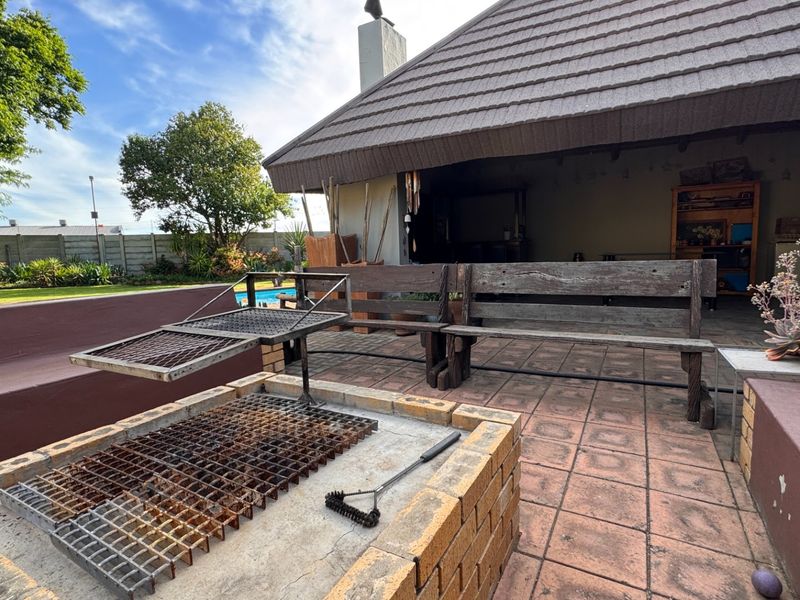 Outdoor covered patio area featuring a built-in brick braai, tiled flooring, and direct access to the garden and pool area.