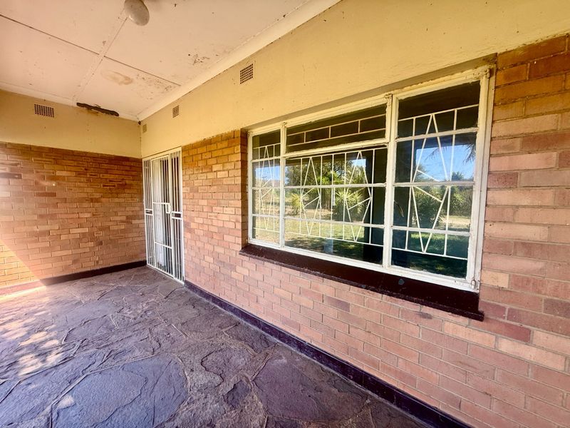 A covered patio area featuring exposed brick walls, stone flooring, and security bars on the windows, showing signs of wear on the ceiling.