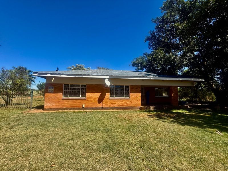A single-story brick house featuring a corrugated metal roof, security window bars, and a front lawn area.