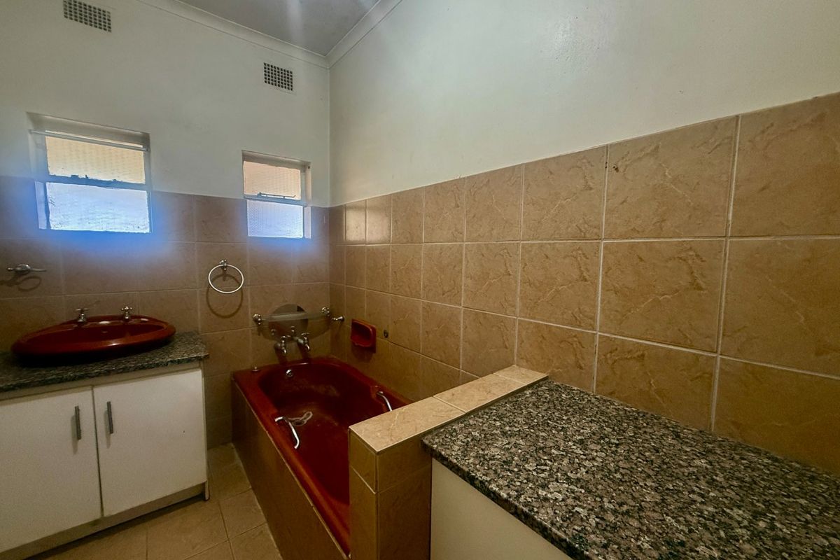 A dated bathroom featuring a built-in vanity with granite countertop, tiled bathtub, and neutral wall tiling, offering potential for a modern renovation.