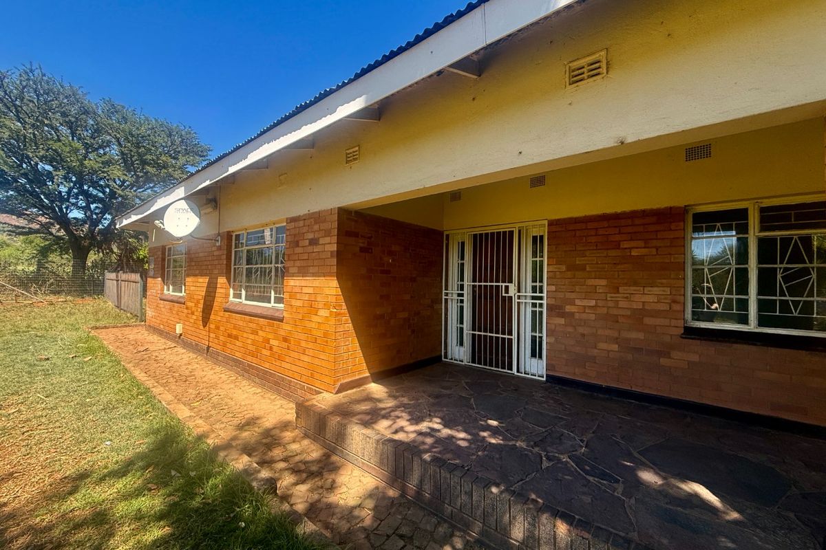 Rear view of a face brick house featuring a stone-paved patio, security gate, and steel window frames under a corrugated metal roof.