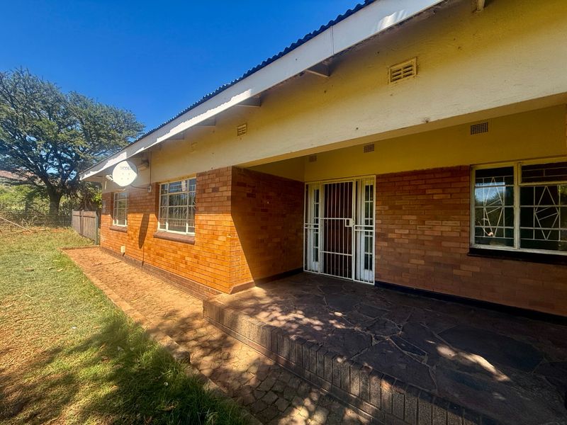 Rear view of a face brick house featuring a stone-paved patio, security gate, and steel window frames under a corrugated metal roof.