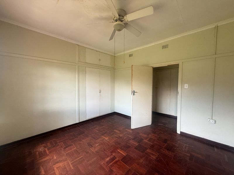 An empty bedroom featuring original parquet flooring, built-in cupboards, and a ceiling fan, offering a blank canvas for renovation.