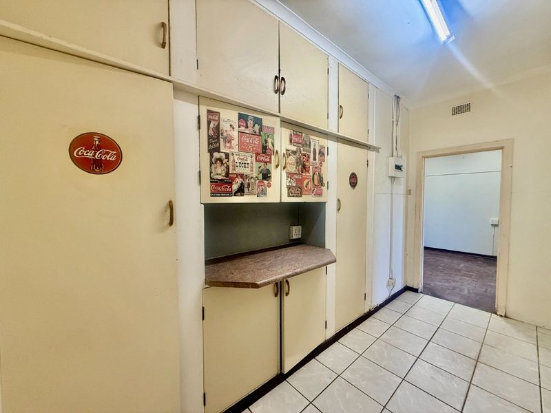 A functional scullery or utility area featuring extensive built-in cabinetry, laminate countertops, and tiled flooring, offering ample storage space for household needs.