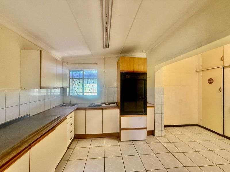 A dated kitchen featuring built-in cabinetry, an integrated oven and hob, tiled flooring, and a functional layout ready for modernization.