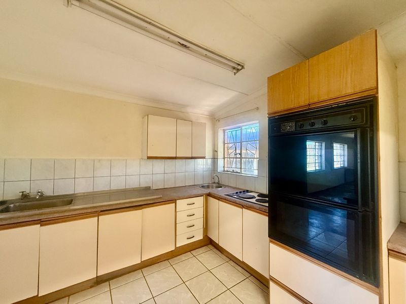 A functional kitchen featuring built-in cabinetry, a double sink, an integrated oven, and an electric hob, offering a blank canvas for modern renovation.