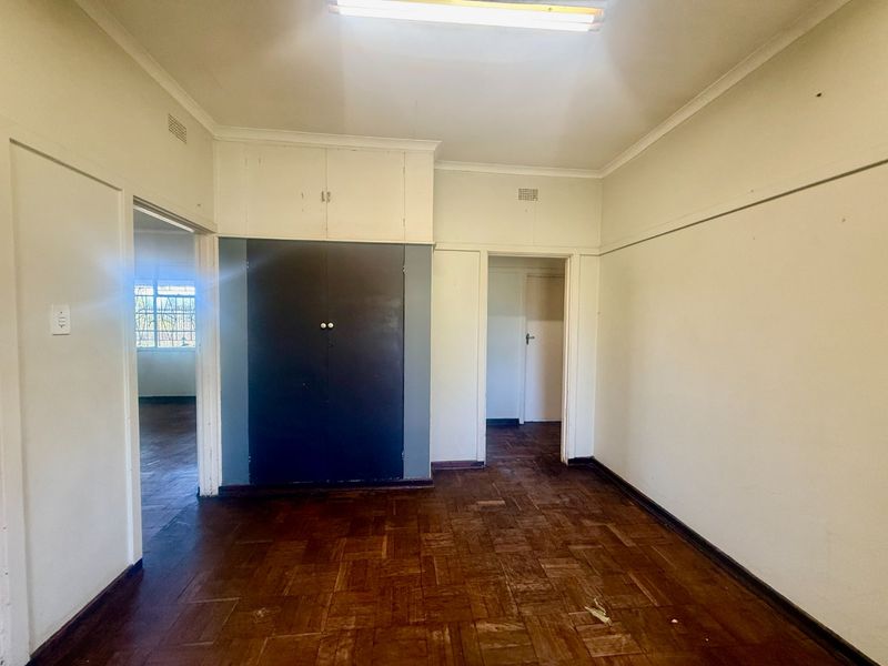An empty bedroom featuring original parquet flooring, built-in cupboards, and neutral wall finishes, offering a blank canvas for renovation.