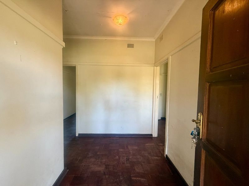 An empty entrance hall featuring original parquet flooring, a timber door, and neutral wall finishes, providing a blank canvas for interior updates.