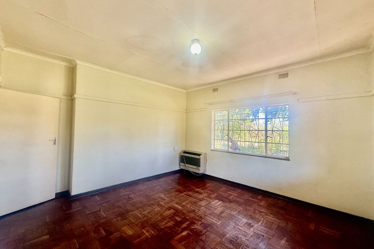 An empty bedroom featuring original parquet flooring, a window with security bars, and a wall-mounted air conditioning unit.