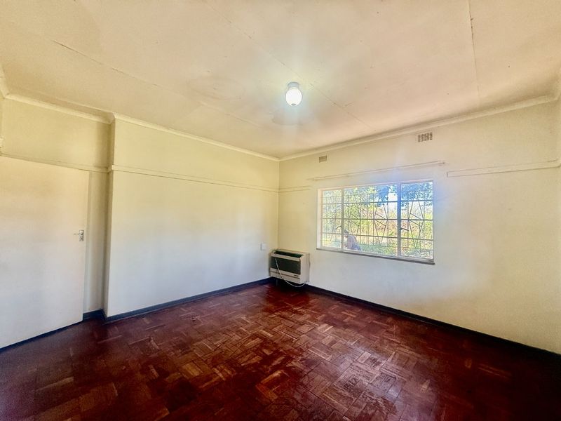 An empty bedroom featuring original parquet flooring, a window with security bars, and a wall-mounted air conditioning unit.
