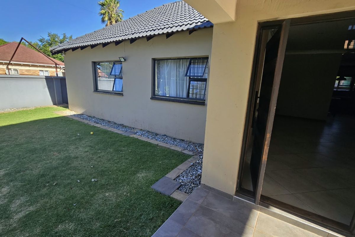Rear view of the property featuring a tiled patio, lawn area, and perimeter wall, with direct access to the interior living space.