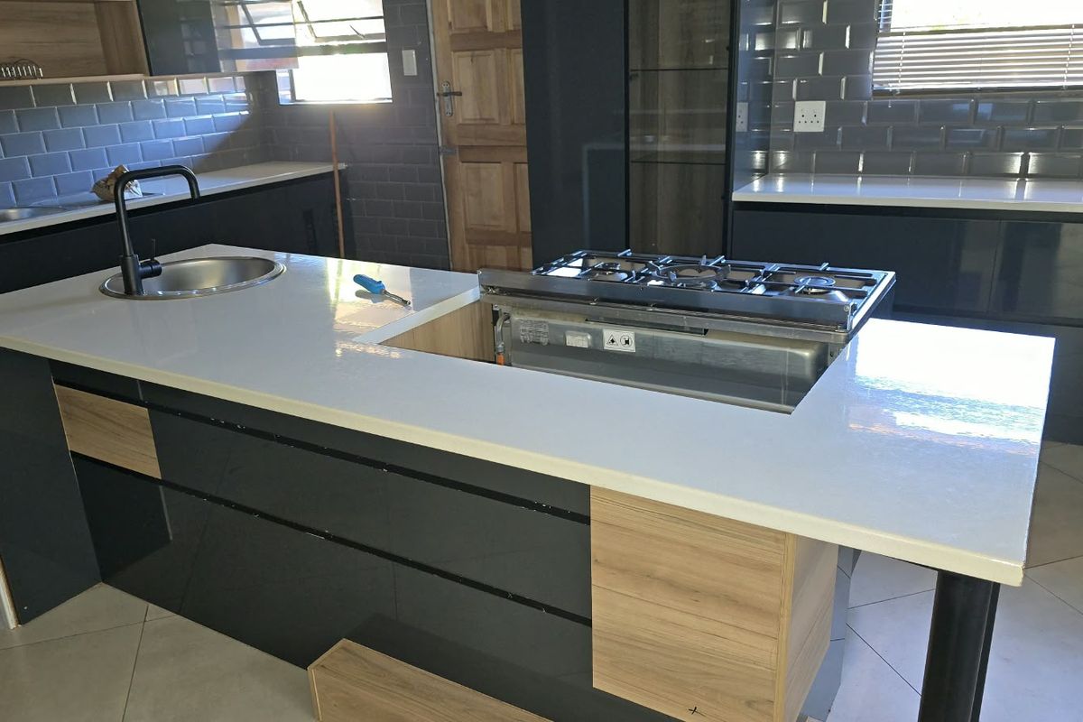 Modern kitchen featuring a central island with a gas hob, quartz countertops, and dark cabinetry with subway tile backsplash, currently awaiting final installation.
