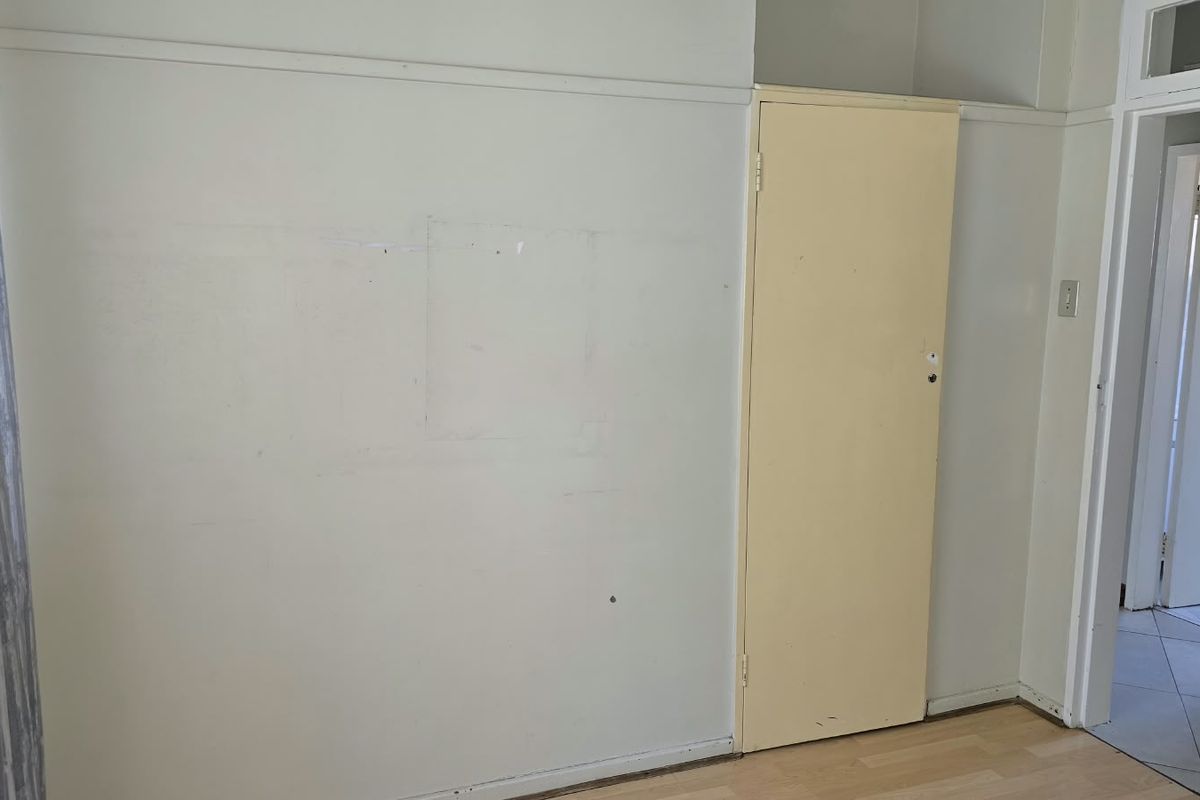 An empty bedroom featuring laminate flooring and a built-in cupboard, requiring minor cosmetic updates to the walls and door.