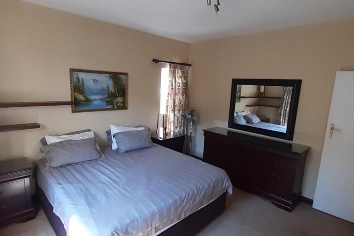 A standard bedroom featuring neutral wall tones, carpeted flooring, and built-in wall shelving.