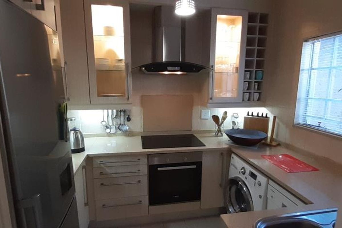 A compact, well-equipped kitchen featuring modern cabinetry, integrated appliances, an electric hob, extractor fan, and built-in oven with efficient under-cabinet lighting.