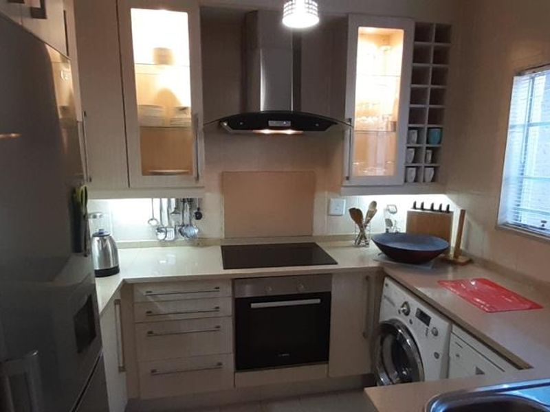 A compact, well-equipped kitchen featuring modern cabinetry, integrated appliances, an electric hob, extractor fan, and built-in oven with efficient under-cabinet lighting.