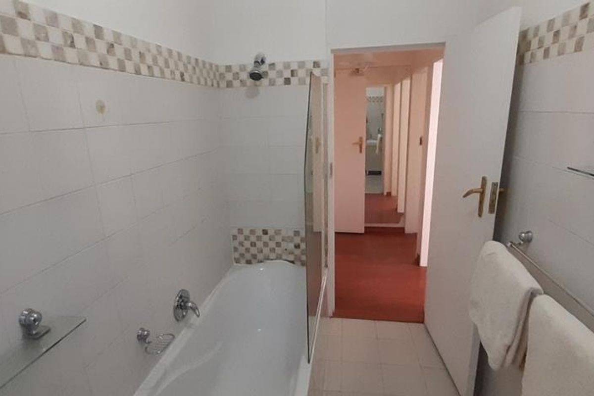 A functional bathroom featuring a bathtub with shower head, tiled walls with decorative border, and built-in glass shelving.